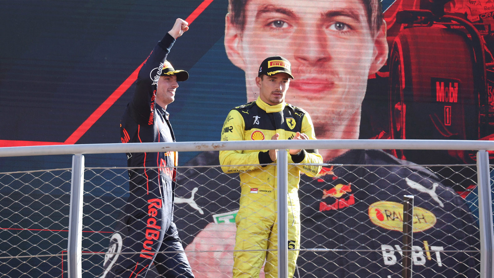 Charles Leclerc applauds as Max Verstappen holds his arm up on the podium after winning the 2022 Italian Grand Prix