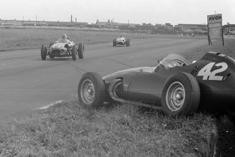 Roy Salvadori (Aston Martin DBR4/250) ahead of Chris Bristow (Cooper T51 Borgwar) pass Ron Flockhart's abandoned BRM P25.