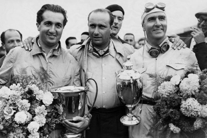 Juan Fangio stands between Alberto Ascari and Guiseppe Farina who hold their trophies and bouquets after the auto race at Silverstone.