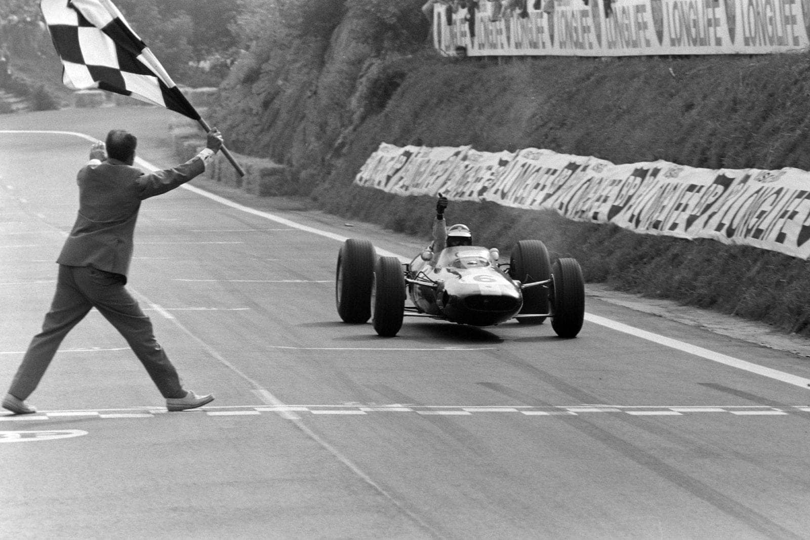 Jim Clark, Lotus 25 Climax, gives a thumbs up as he takes the chequered flag.