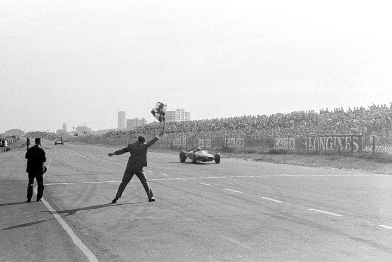 Race winner Jack Brabham (AUS) Brabham BT19 takes the chequered flag to score his hat-trick of consecutive victories.
