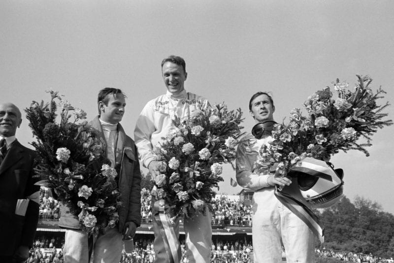Dan Gurney, 1st position, Jackie Stewart, 2nd position, and Chris Amon, 3rd position, celebrate on the podium.