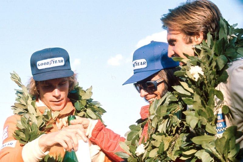 Emerson Fittipaldi is flanked by James Hunt (left) and Carlos Reutemann (right) on the podium.