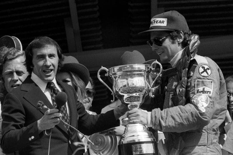 Niki Lauda (Ferrari) is handed the trophy by Jackie Stewart at the 1976 South African Grand Prix.