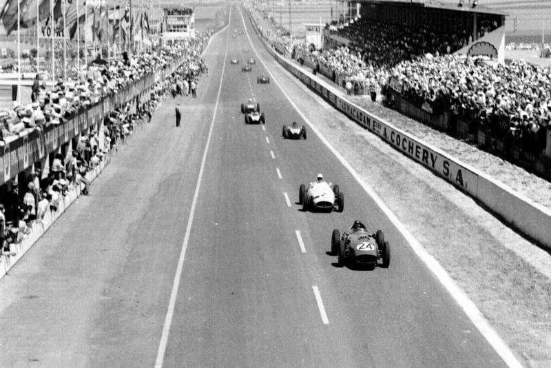 Tony Brooks (Ferrari Dino 246) leads Stirling Moss (BRM P25) and the field past the grandstands and pits.