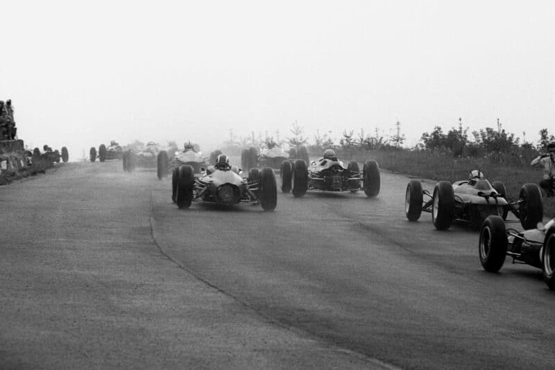 The competitors climb through Eau Rouge in tricky wet conditions at the start; a keen photographer on the right getting very close to the action.