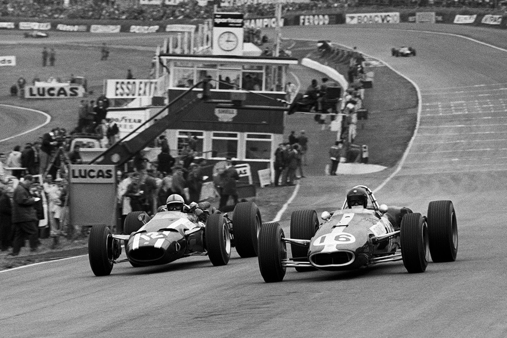 (L to R): Race retiree John Surtees in a Cooper T81 moves to pass fellow retiree Dan Gurney in his Eagle T1G under braking into Paddock Hill Bend.