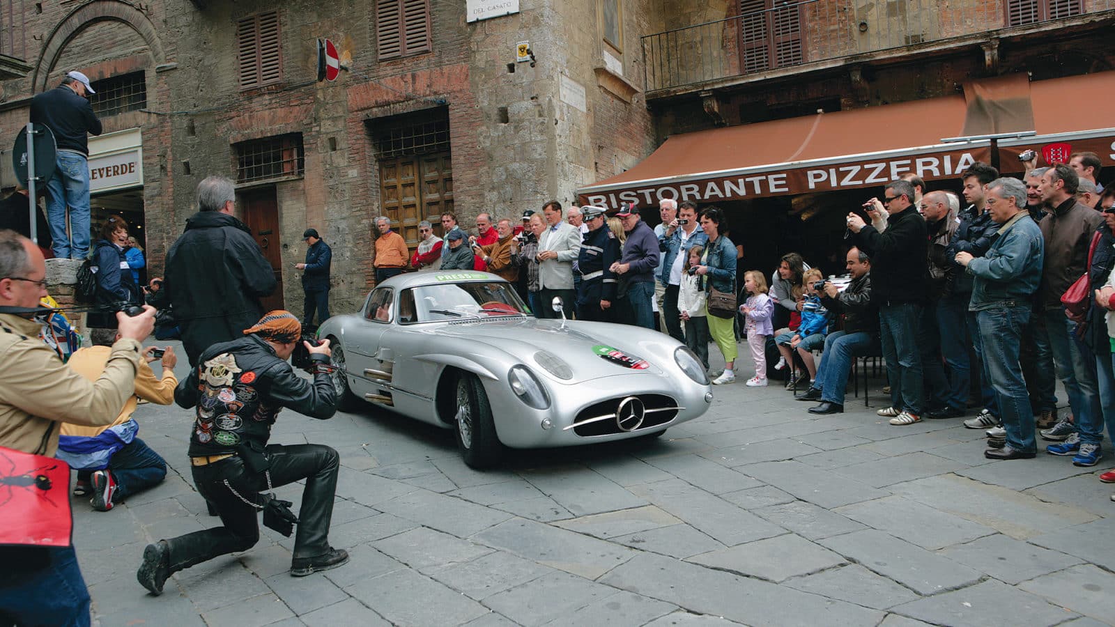 A crowd watches Mercedes 300 SLR Coupe driving through town in the 2010 Mille Miglia