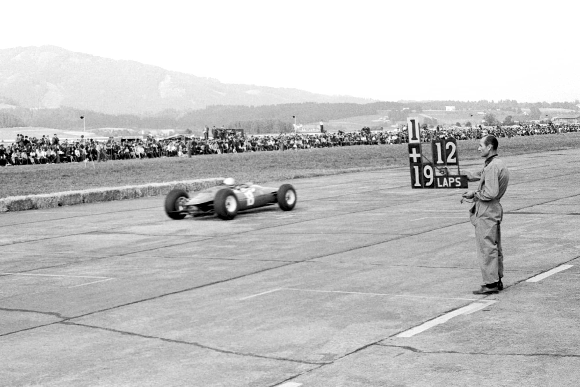 Pit crew member holds out a pit board for Bandini.