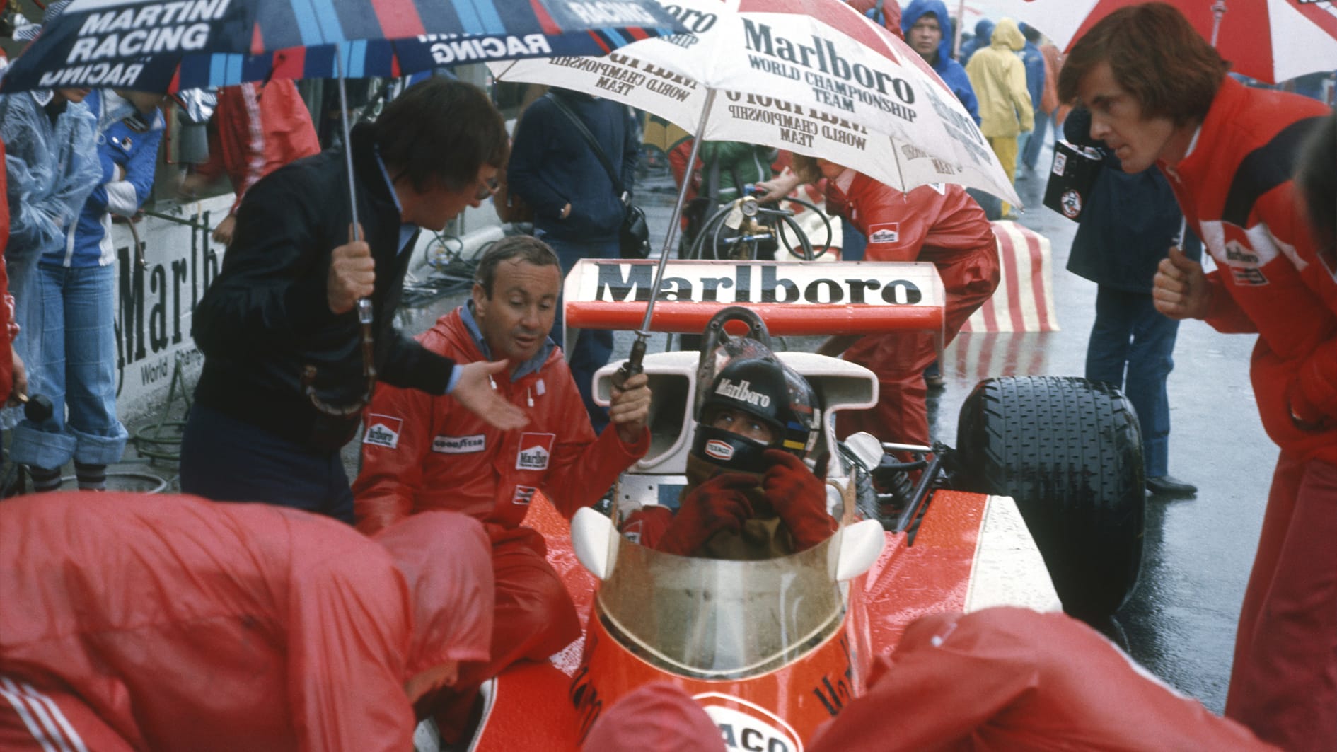 Bernie Ecclestone with Teddy Mayer and Alistair Caldwell around James Hunt in cockpit of McLaren