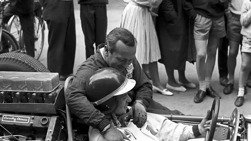 Colin Chapman with arm around Jim Clark who is sitting in Lotus cockpit