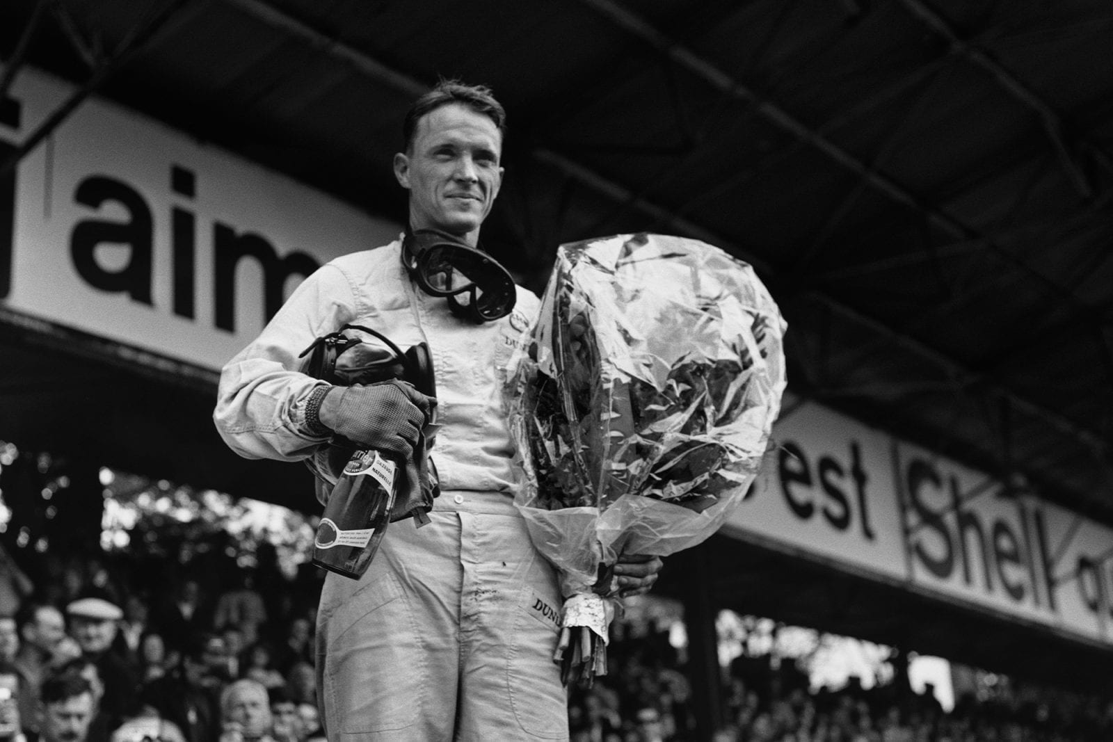 Brabham's Dan Gurney stands on the podium, champagne and bouquet in hand.