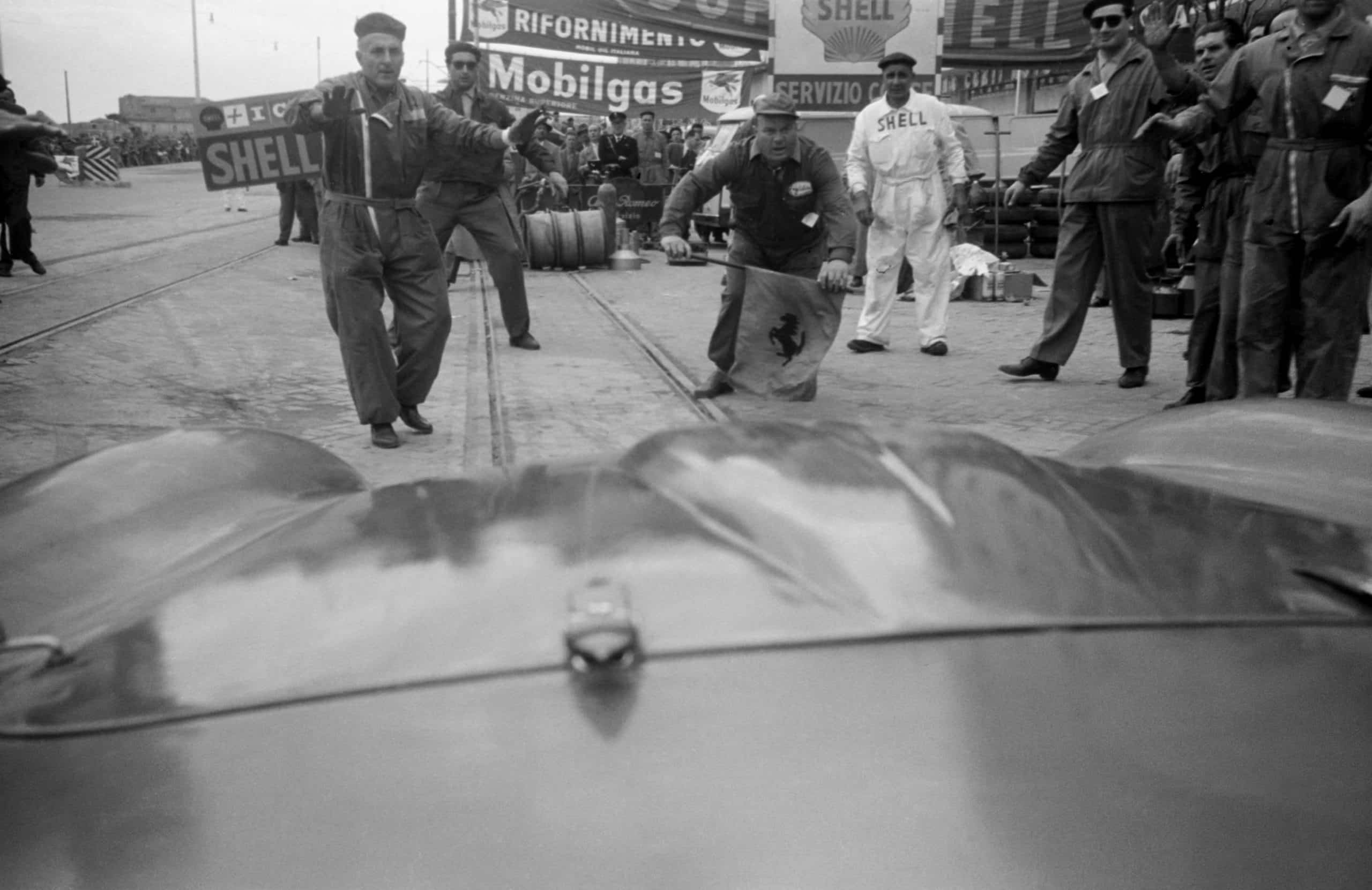 The Ferrari driven by Peter Collins and Louis Klemantaski arrives in the pit lane for refuelling during the Mille Miglia, April 1956. Louis Klemantaski: 'Coming in at high speed for our second refuelling, my heart stopped when the waiting mechanics were about to be annihilated. But such was their faith that they stood their ground and we halted just as the bonnet touched Parenti?s flag.' (Photo by Klemantaski Collection/Getty Images)