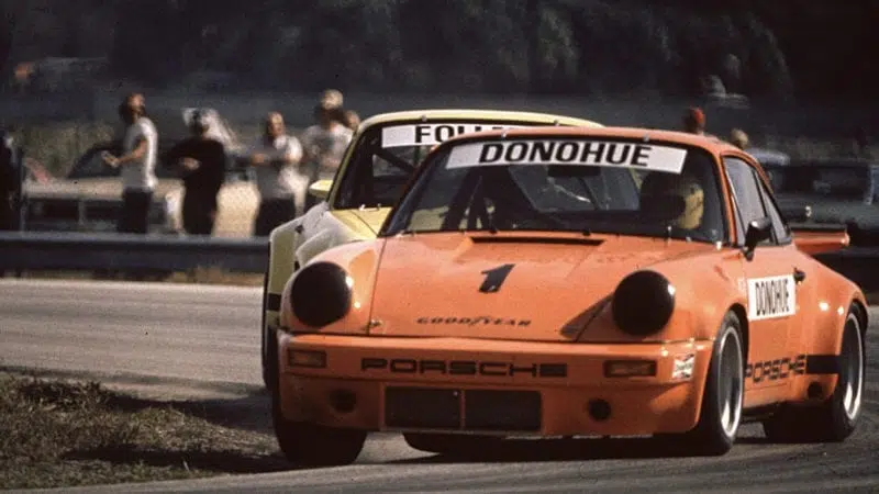 Mark Donohue racing an orange Porsche 911 RSR at Riverside in the 1973 International Race of Champions season
