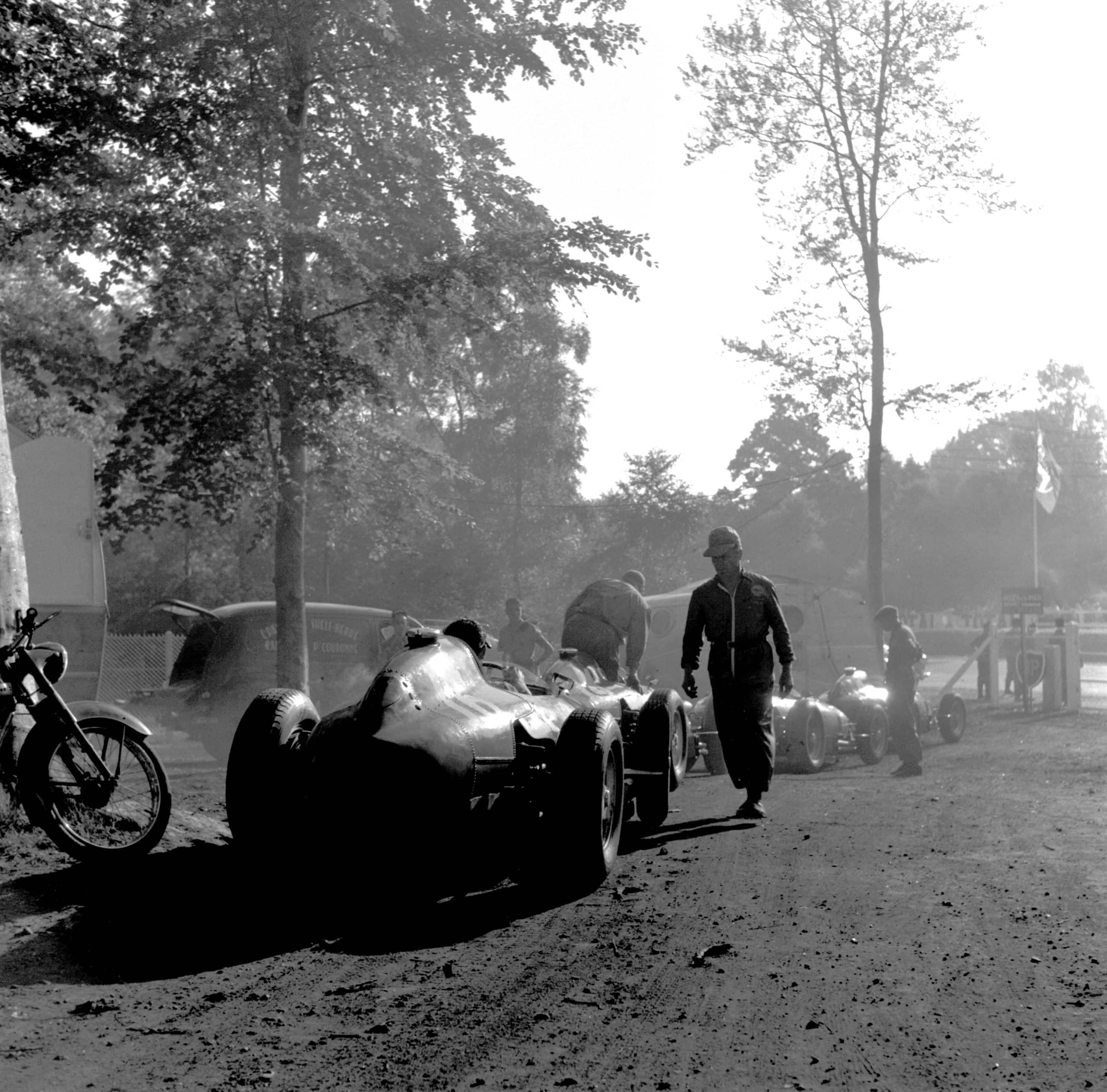 The French Grand Prix; Rouen-les Essarts, July 7, 1957. Early morning in the Rouen paddock which was in a lovely grove of pines � the Ferraris are in line to be fueled before the start. Car n. 16 was to be driven by the FrenchmanMaurice Trintignant, but did not finish. Once again Klemantaski uses the natural composition of the surroundings in early morning to evoke the silence before the thunder of the coming race. In the race itself, Fangiowas totally dominant in his Maserati 250F, presaging his astounding victory at the Nürburgring which would come a month later. Starting from pole position, he finished almost a minute ahead of Musso�s Ferrari. (Photo by Klemantaski Collection/Getty Images)