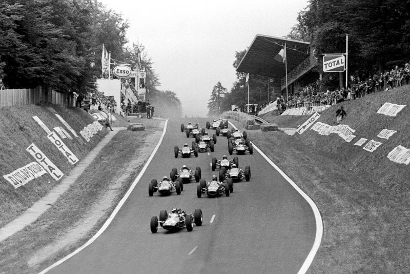 Jim Clark, Lotus 25 Climax, leads Dan Gurney, Brabham BT7 Climax, and John Surtees, Ferrari 158, as the field follow behind.