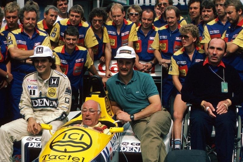 BBC TV commentator Murray Walker in the Williams FW11 sits with the regular drivers Nelson Piquet (left) and Nigel Mansell. Team Owner Frank Williams sits to the right.