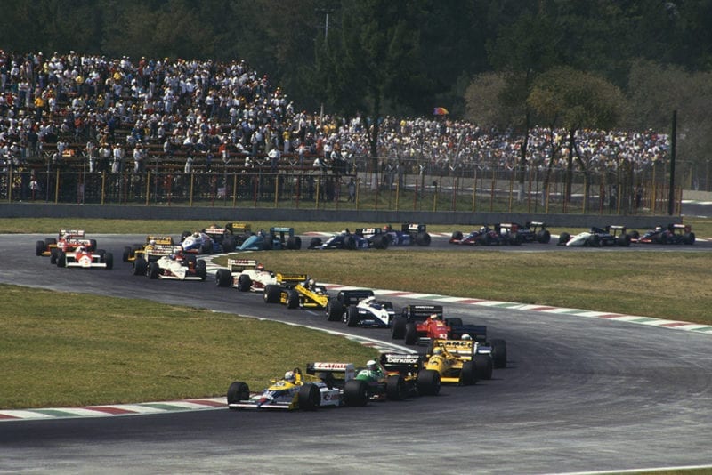 Nigel Mansell (Williams FW11B Honda) 1st position, leads Teo Fabi (Benetton B187 Ford), Ayrton Senna (Lotus 99T Honda) and the rest of the field on the first lap of the Mexican GP.