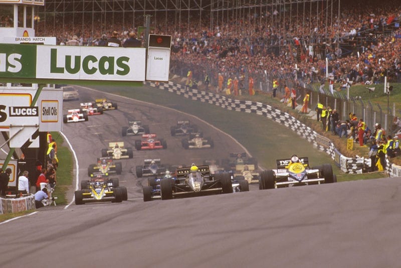 Ayrton Senna (Lotus 97T Renault) leads Nigel Mansell (Williams FW10 Honda) on the climb upto Paddock Hill Bend at the start.