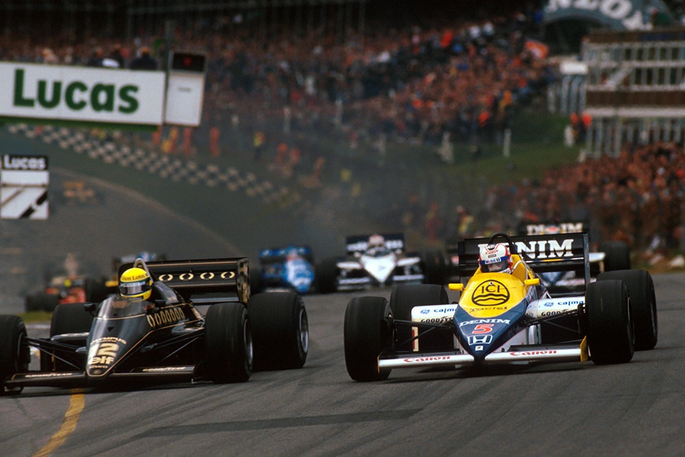 Nigel Mansell in his Williams FW10 challenges pole sitter Ayrton Senna in a Lotus 97T into Paddock Hill Bend.