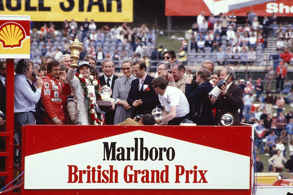 Alan Jones (Williams Ford) celebrates his 1st position on the podium. TRH Prince and Princess Michael of Kent stand to the right and Carlos Reutemann (Williams Ford) 3rd position and commentator Brian Jones to the left.