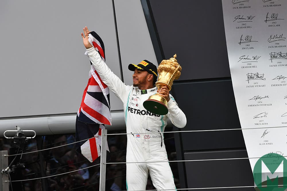 Lewis Hamilton holds the race-winning 2019 British Grand prix trophy and Union jack on the podium