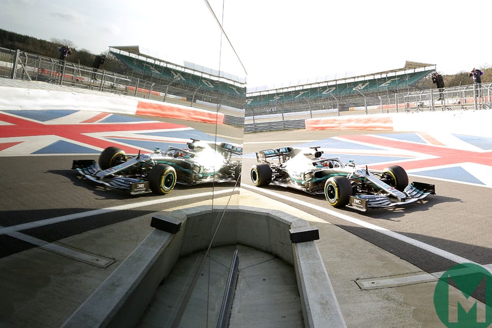 Lewis Hamilton's Mercedes F1 car drives past the glass of Silverstone's Wing, generating a mirror image