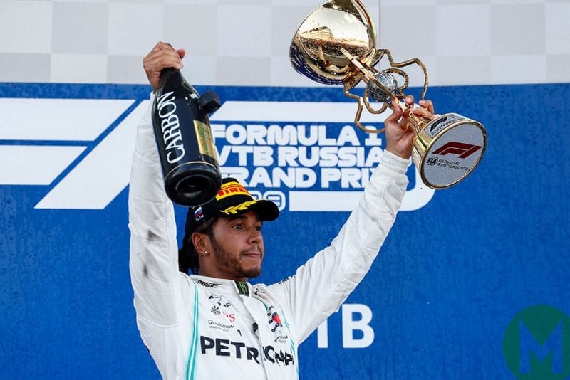 Lewis Hamilton celebrates victory at the 2019 Russian Grand Prix, with champagne in one hand and his trophy in the other