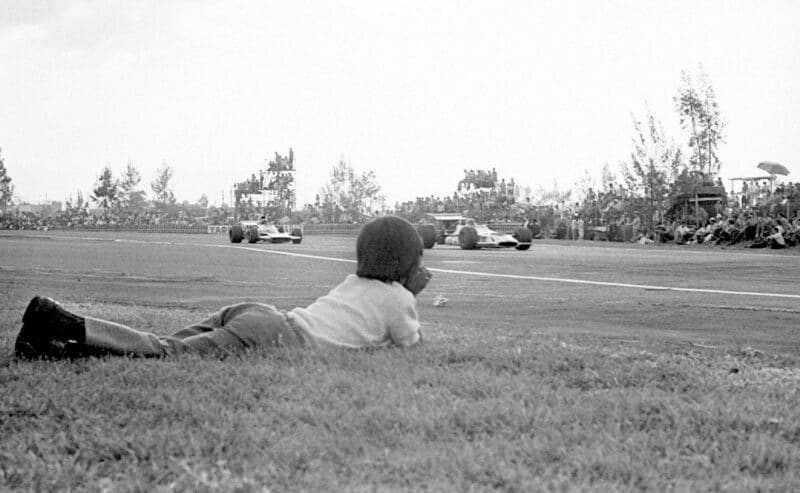 A boy lies on the trackside grass watching the 1970 Mexican Grand Prix