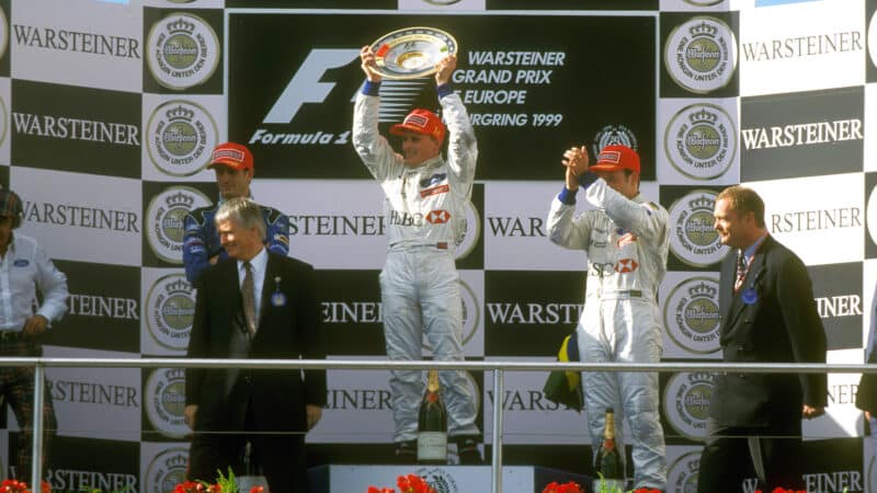 Johnny-Herbert-celebrates-1999-European-Grand-Prix-in-for-Stewart-Grand-Prix-holding-up-trophy-on-the-podium