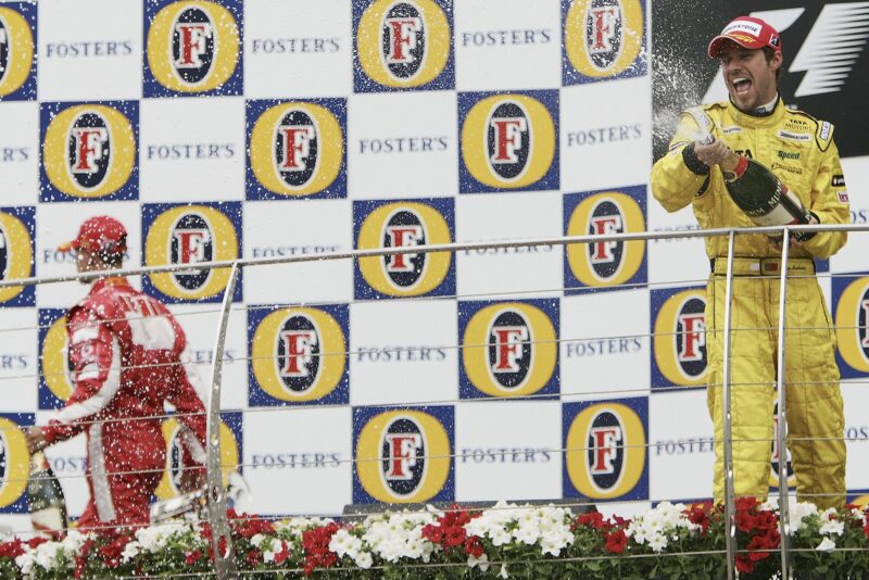 Tiago Monteiro sprays champagne as Michael Schumacher walks off the podium at the 2005 US Grand Prix