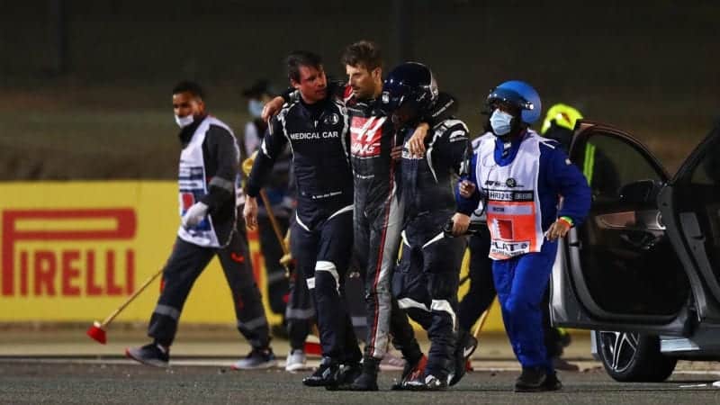 Romain Grosjean is lead away from the burnt wreckage of his car after crashing at the 2020 F1 Bahrain Grand Prix