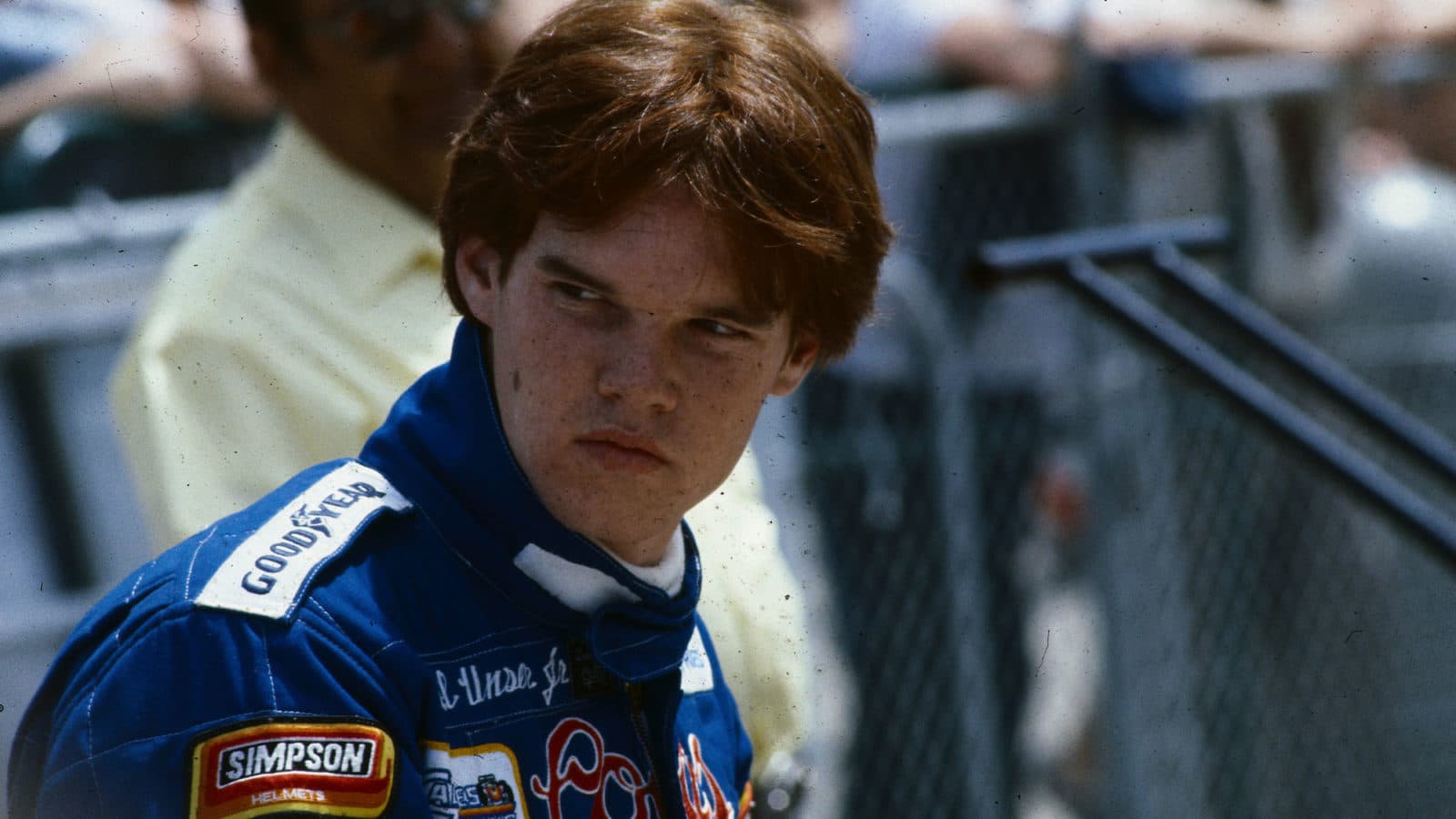 1983- Close-up of Indy 500 race car driver Al Unser Jr, standing alone in front of a crowd at the side of a racetrack. Photo filed 5/14/1983.