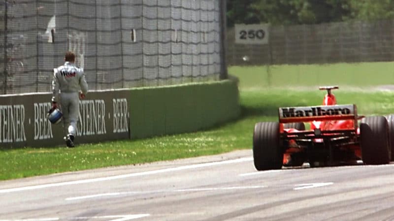 Ferrari of Michael Schumacher drives past a walking Mika Hakkinen in the 1999 San Marino GP
