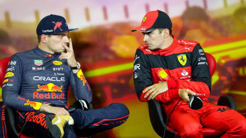 Max Verstappen holds his fingers in a v shape as he and Charles Leclerc grimace