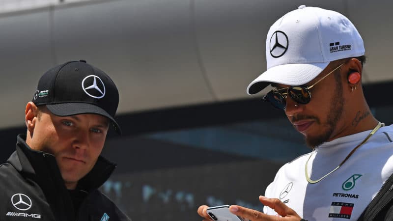 Valtteri Bottas stands next to LEwis Hamilton who is looking at his phone