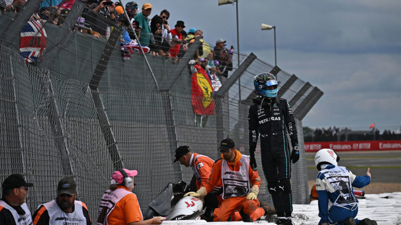 TOPSHOT - Mercedes' British driver George Russell (2R) stands with officials as they work to free Alfa Romeo Chinese driver Zhou Guanyu from his car, lodged in the crash barrier after an incident at the start of the Formula One British Grand Prix at the Silverstone motor racing circuit in Silverstone, central England on July 3, 2022. (Photo by Ben Stansall / AFP) (Photo by BEN STANSALL/AFP via Getty Images)
