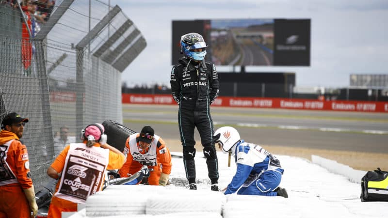 George Russell stands on the tyre barrier to check on Zhou Guanyu after their crash at the 2022 British Grand Prix