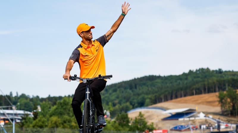 Daniel Ricciardo waves to the crowd as he cycles the Spa Francorchamps track in 2022