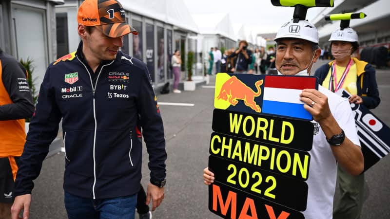 Fans hold up a 2022 world champion pitboard as Max Verstappen walks past at the Japanese Grand Prix