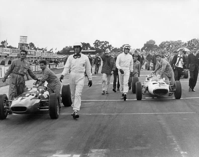 James Garner walks alongside his car while Yves Montand does the same opposite while filming a scene for Grand Prix at Brands Hatch in 1966