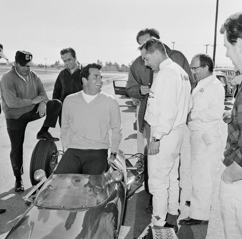 Grand Prix star James Garner slips into a Formula Junior Lotus, dressed up to look like an F1 car, as Phil Hill and director John Frankenheimer look on