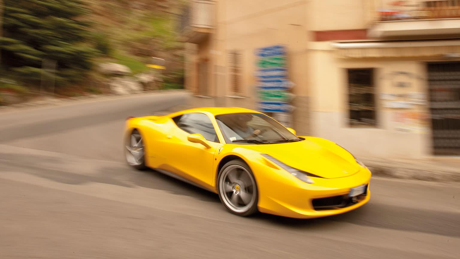 The Ferrari rounds a bend in a village