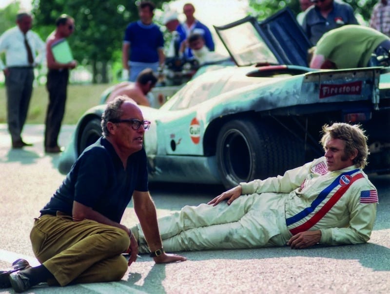 Steve-McQueen-sits-on-the-track-next-to-a-Gulf-Porsche-917-with-le-Mans-director-Lee-Katzin