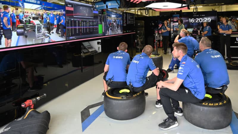 Alpine F1 mechanics sit on tyres in the pit garage