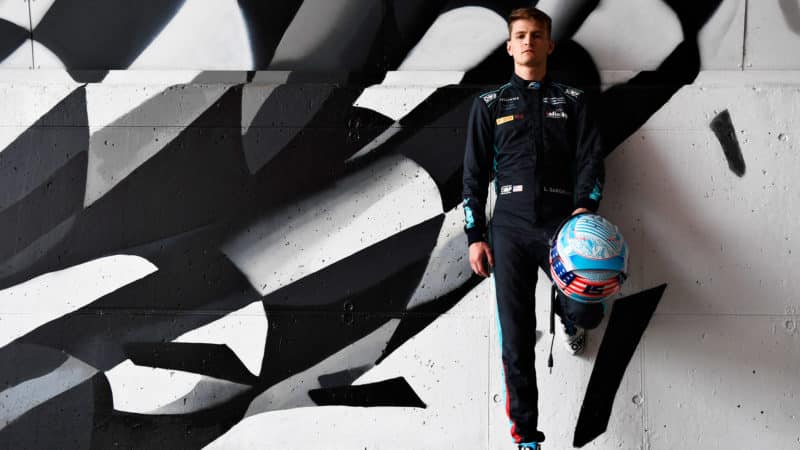Logan Sargeant leqans against a wall with a chequered flag mural