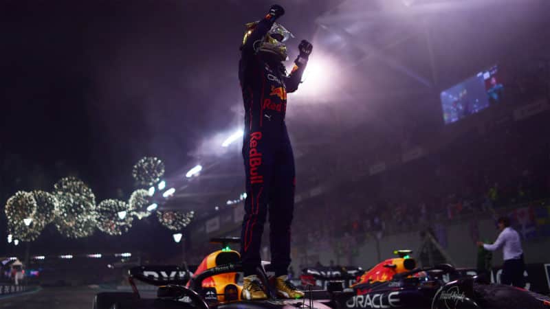 Max Verstappen raises his arms in victory as he stands on his Red Bull after the 2022 Abu Dhabi Grand Prix
