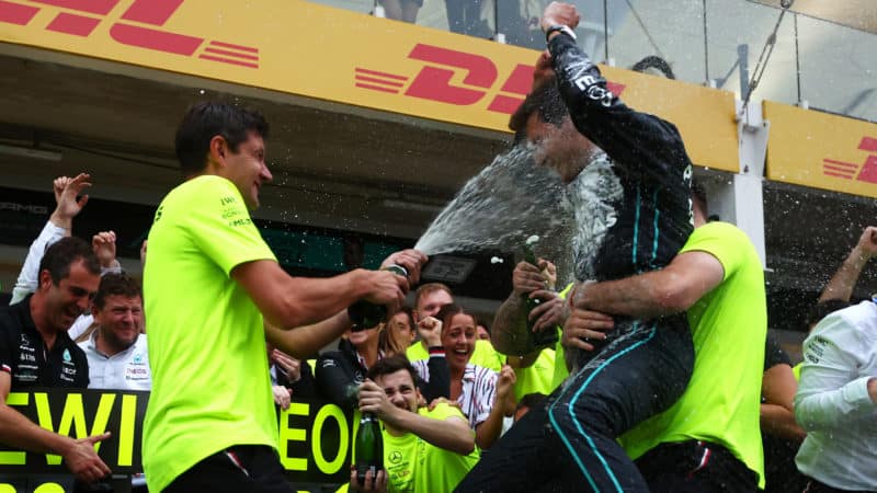 Mercedes team member sprays George Russell with champagne as he is held