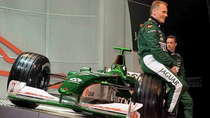 Johnny Herbert sits on front wheel of Jaguar F1 car during 2000 launch
