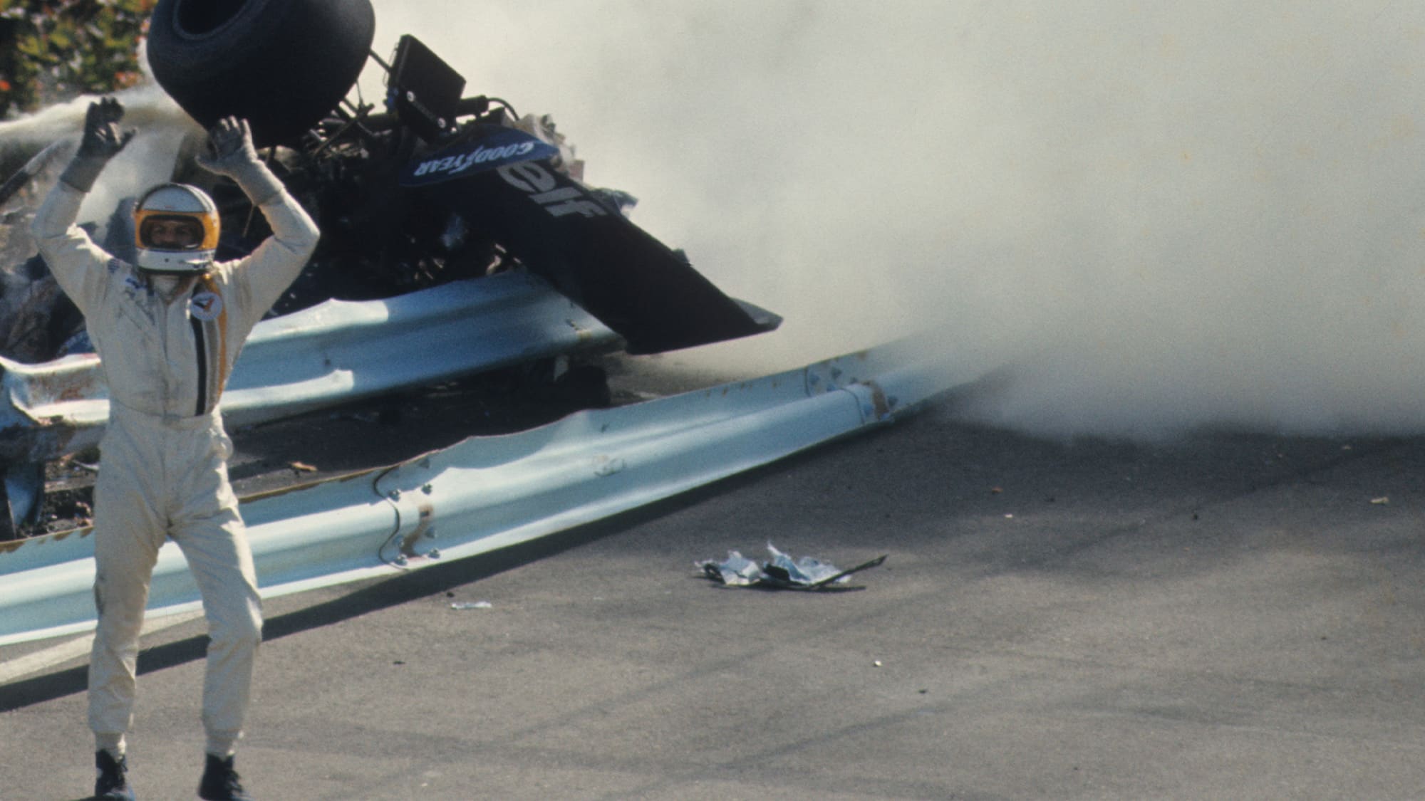 Jody Scheckter waves hios arms at other drivers in front of Francois Cevert wrecked Tyrrell